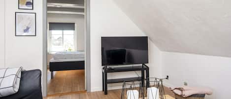 A modern living room with a flat-screen TV, a sofa, a coffee table, and a bed in the background.