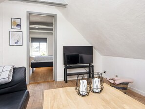 A modern living room with a flat-screen TV, a sofa, a coffee table, and a bed in the background. - 8 Person Holiday Home in Romo (Rømø)