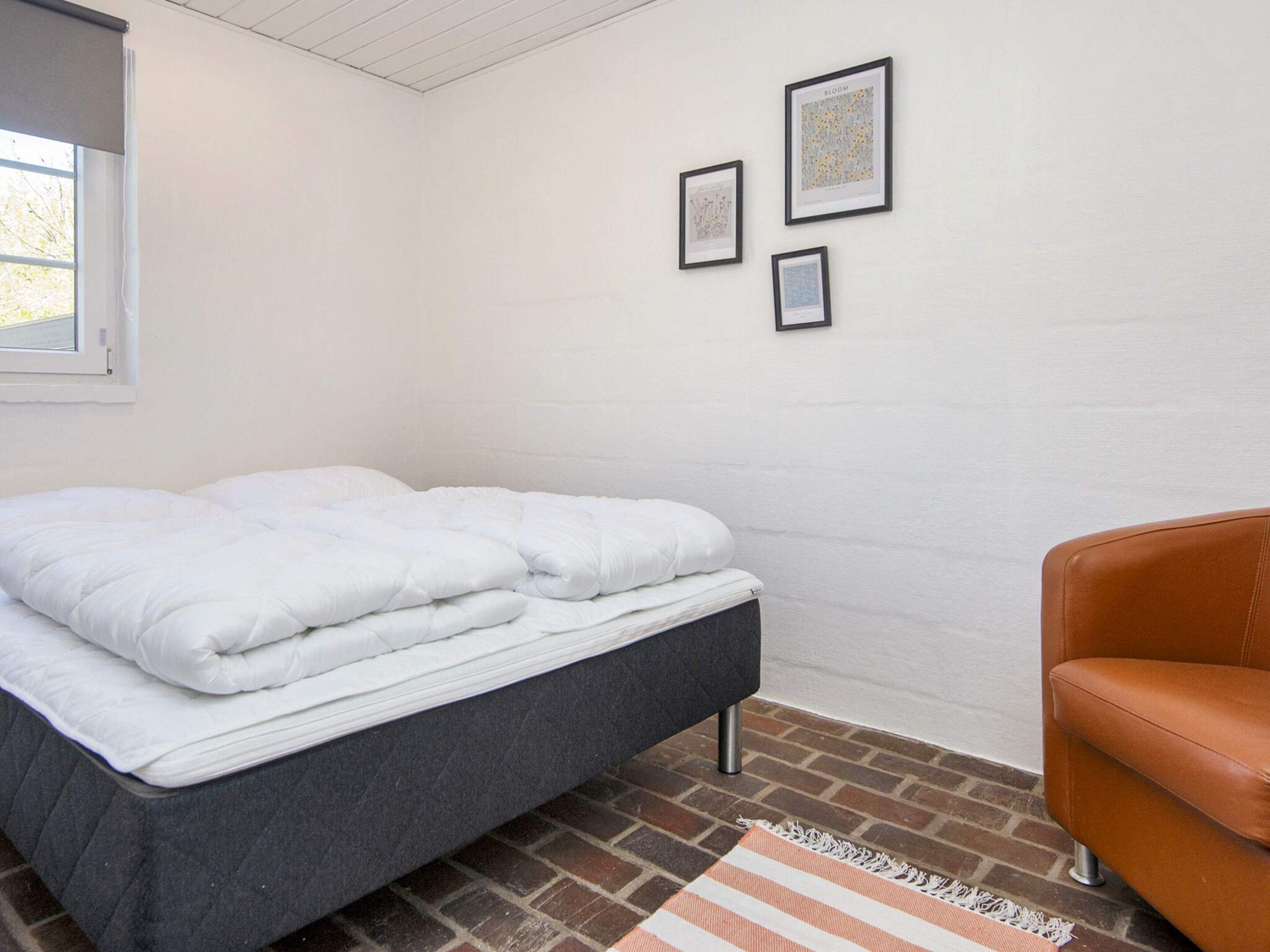 Un dormitorio con una cama, una silla y suelo de ladrillo.