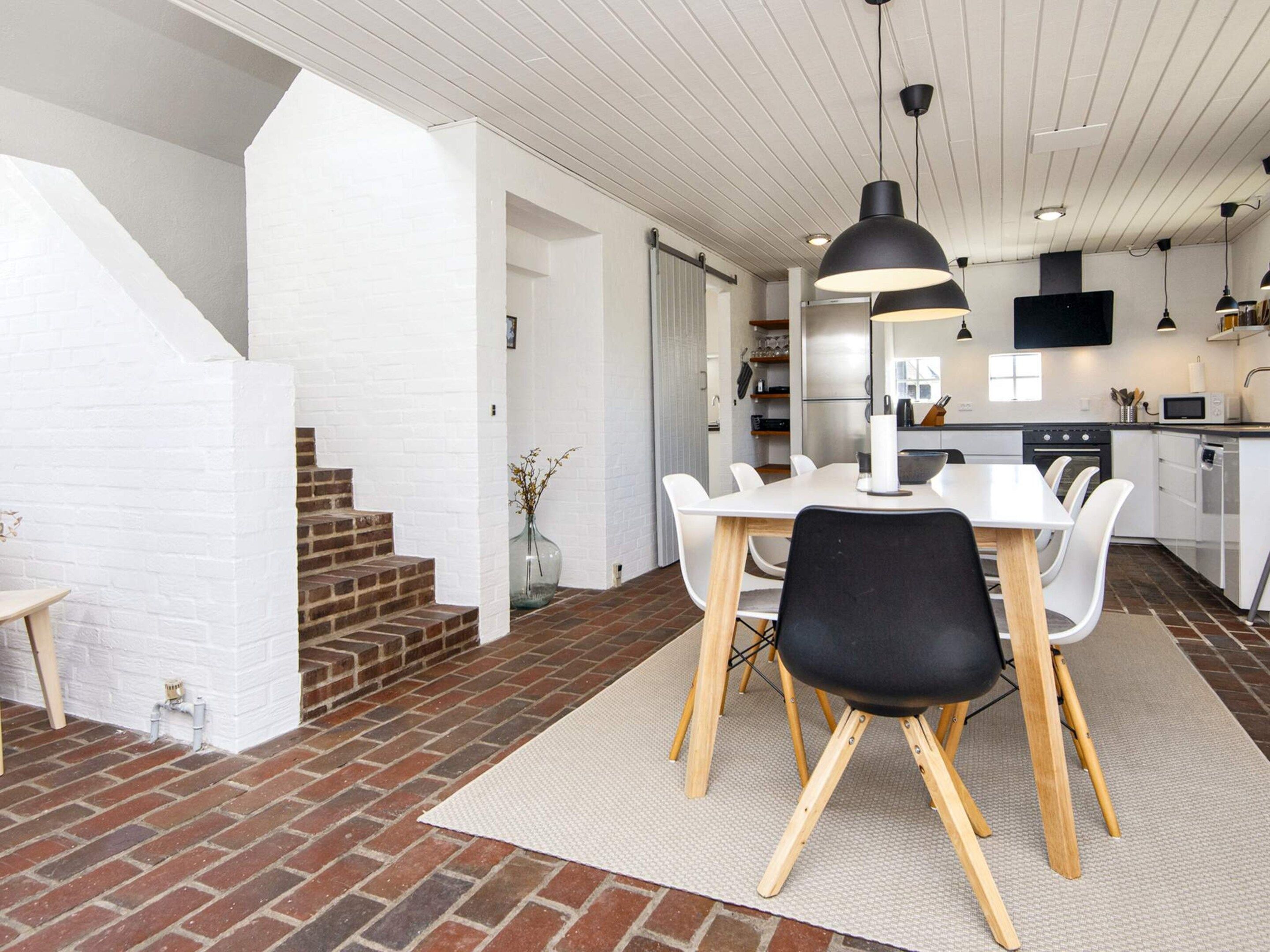 A modern kitchen with white cabinets, a dining area with a white table and chairs, and a brick staircase.