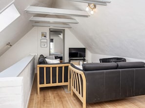 A modern loft bedroom with a sloped ceiling, a wooden bed, a black sofa, and a television. - 8 Person Holiday Home in Romo (Rømø)