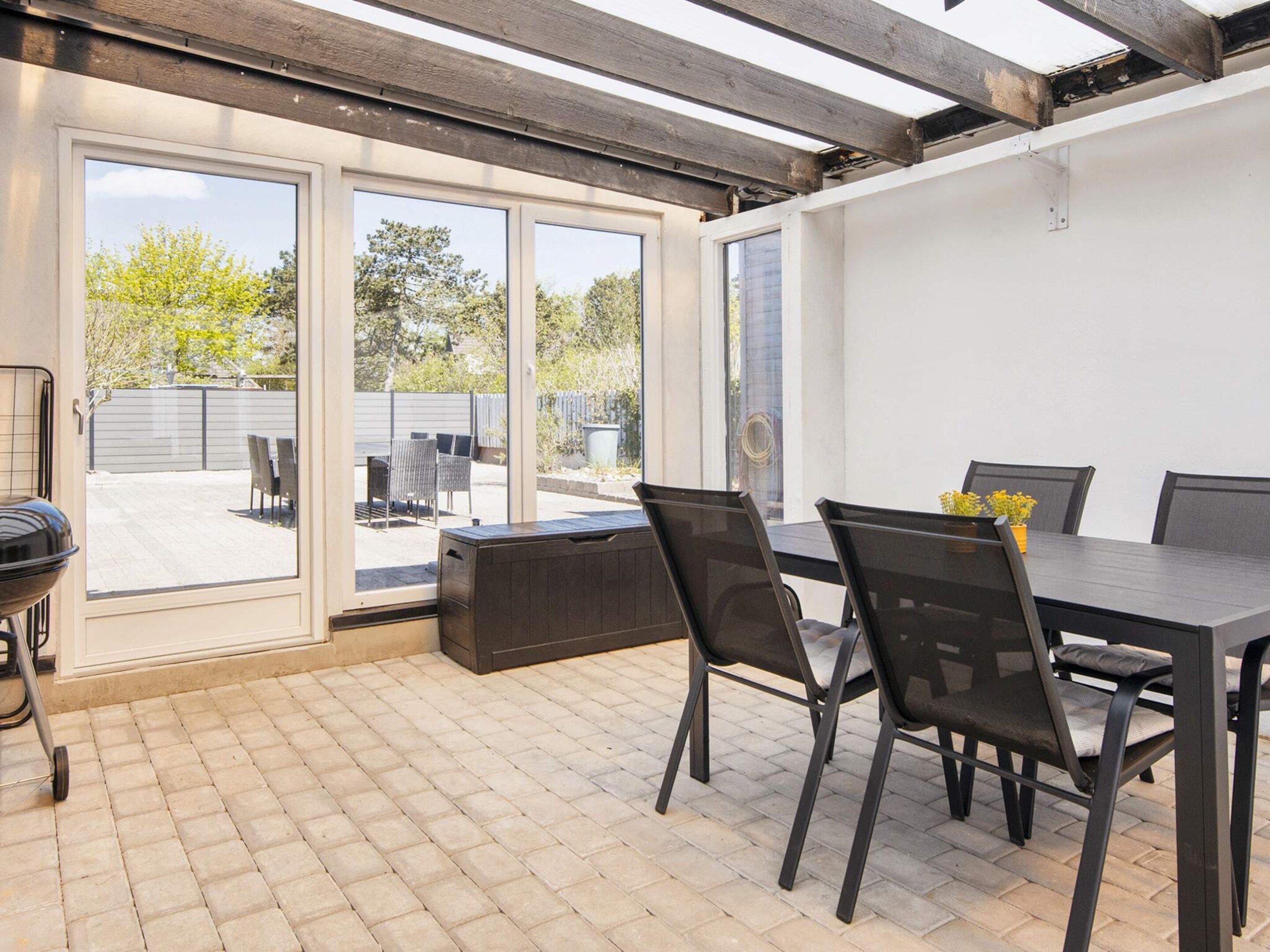 Eine Terrasse mit Tisch, Stühlen, einem Grill und Blick durch Glastüren.
