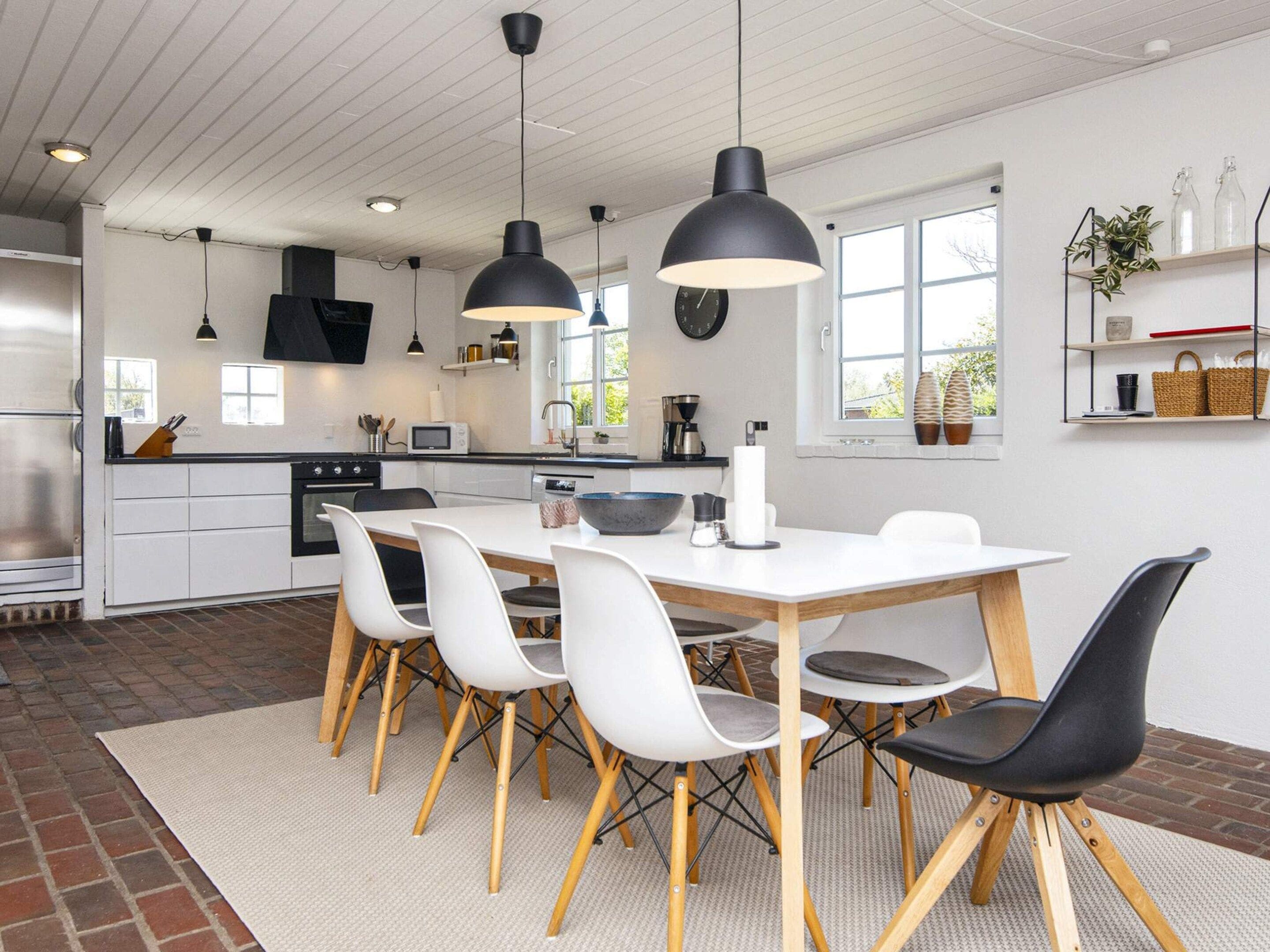A modern kitchen with a central island, white cabinetry, and a dining area with a white table and chairs.