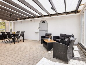 Un patio al aire libre con una mesa, sillas, un sofá y un jarrón decorativo.