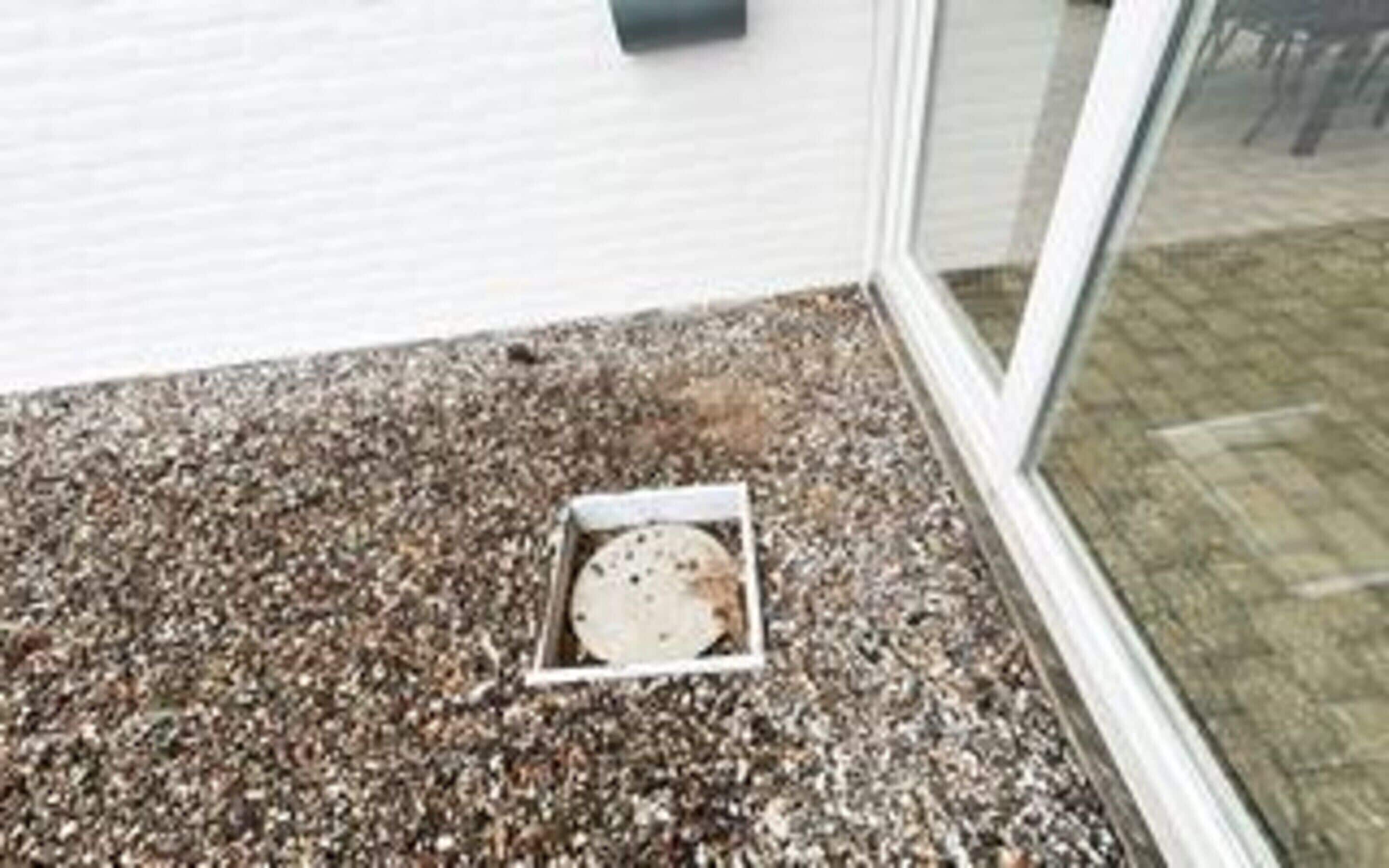 A gravel-covered ground with a white drain cover.