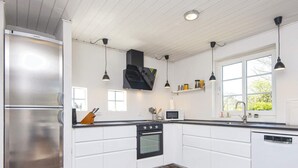 A modern kitchen with white cabinetry, a stainless steel refrigerator, a black range hood, and pendant lighting. - 8 Person Holiday Home in Romo (Rømø)