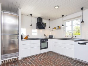Una cocina moderna con armarios blancos, un refrigerador de acero inoxidable, una campana extractora negra e iluminación colgante.