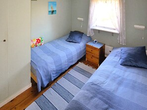 Two single beds with blue striped bedspreads, a wooden nightstand, and a window with a white curtain.