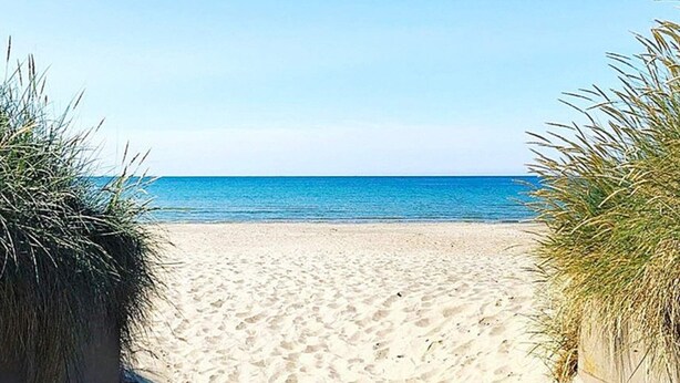 Une plage de sable fin, sous un ciel bleu clair et une mer calme.
