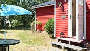 Un bâtiment en bois rouge avec une porte ouverte, une petite table avec un banc, et un parapluie bleu.