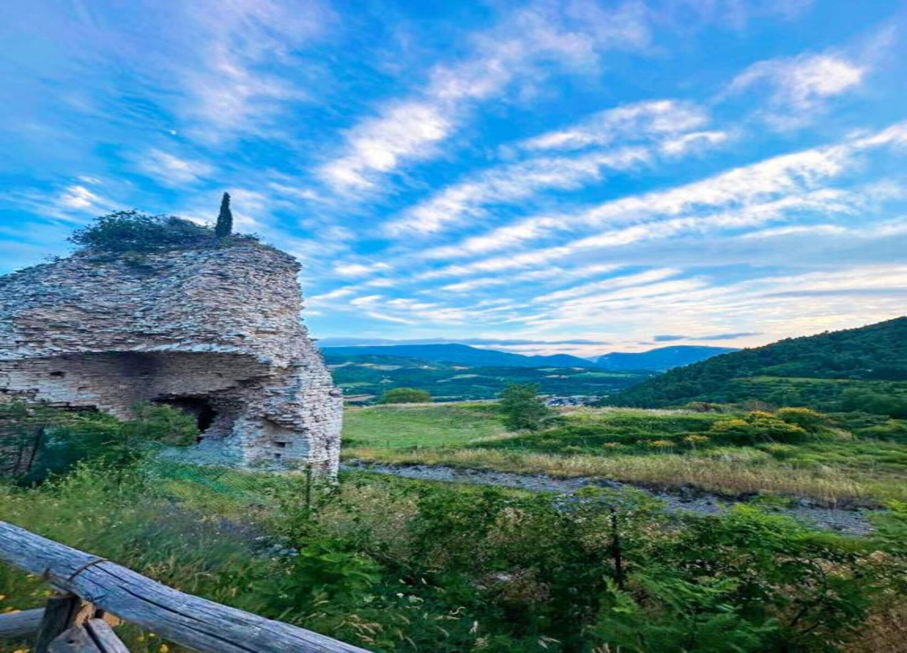 Eine Steinstruktur im Ruin mit Blick auf ein grünes Tal und ferne Berge, der Himmel ist teilweise bewölkt.