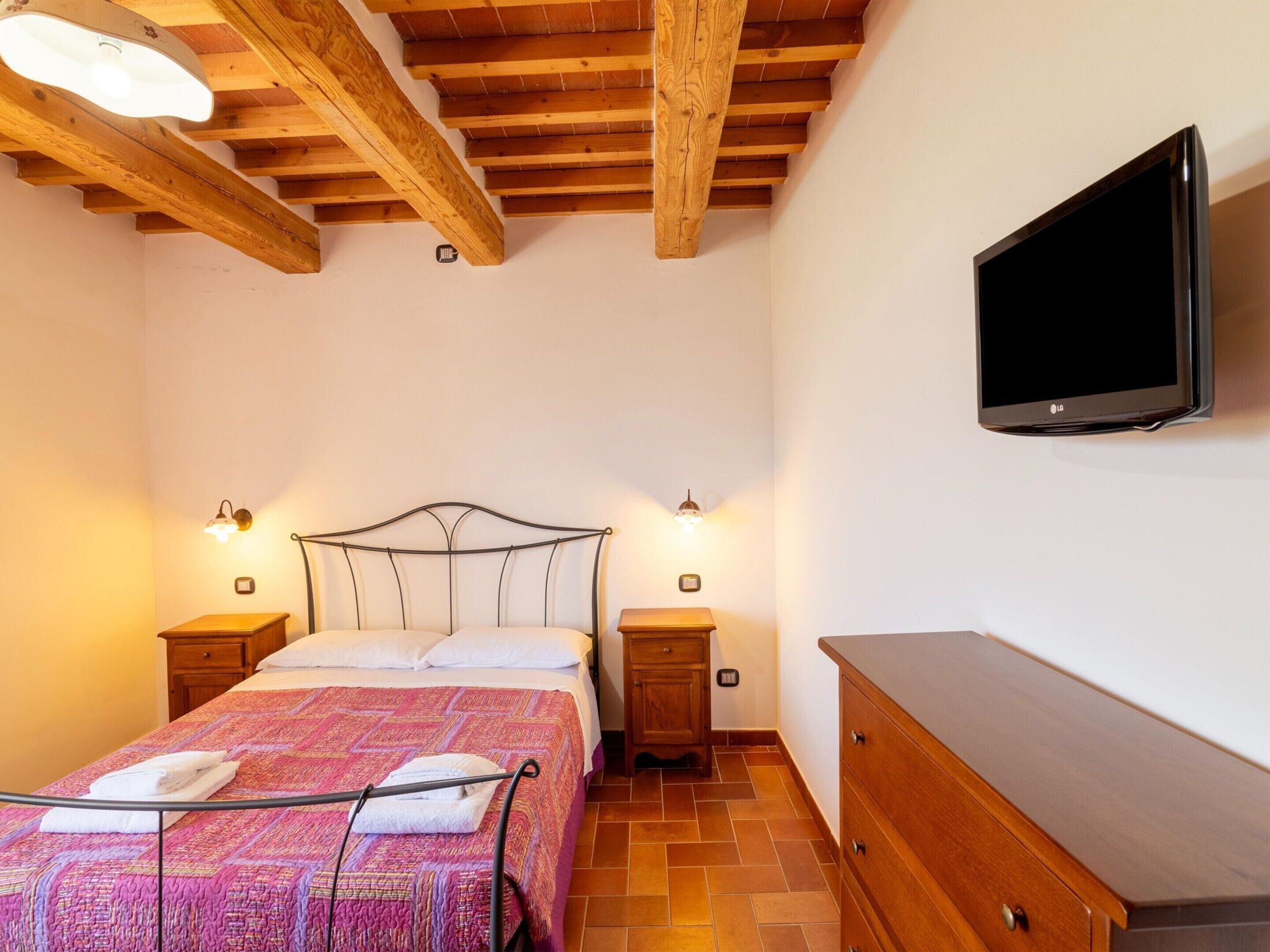 A bedroom with a bed, wooden beams, a TV, bedside lamps, and a dresser.