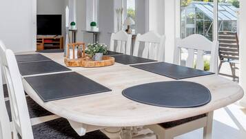Un comedor con una mesa de tonos claros, sillas blancas y individuales negras.