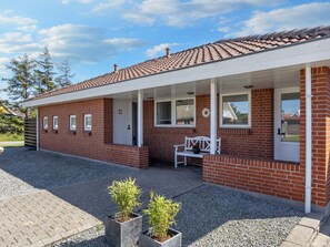 Una casa de ladrillo rojo con un porche blanco, un banco y dos macetas.