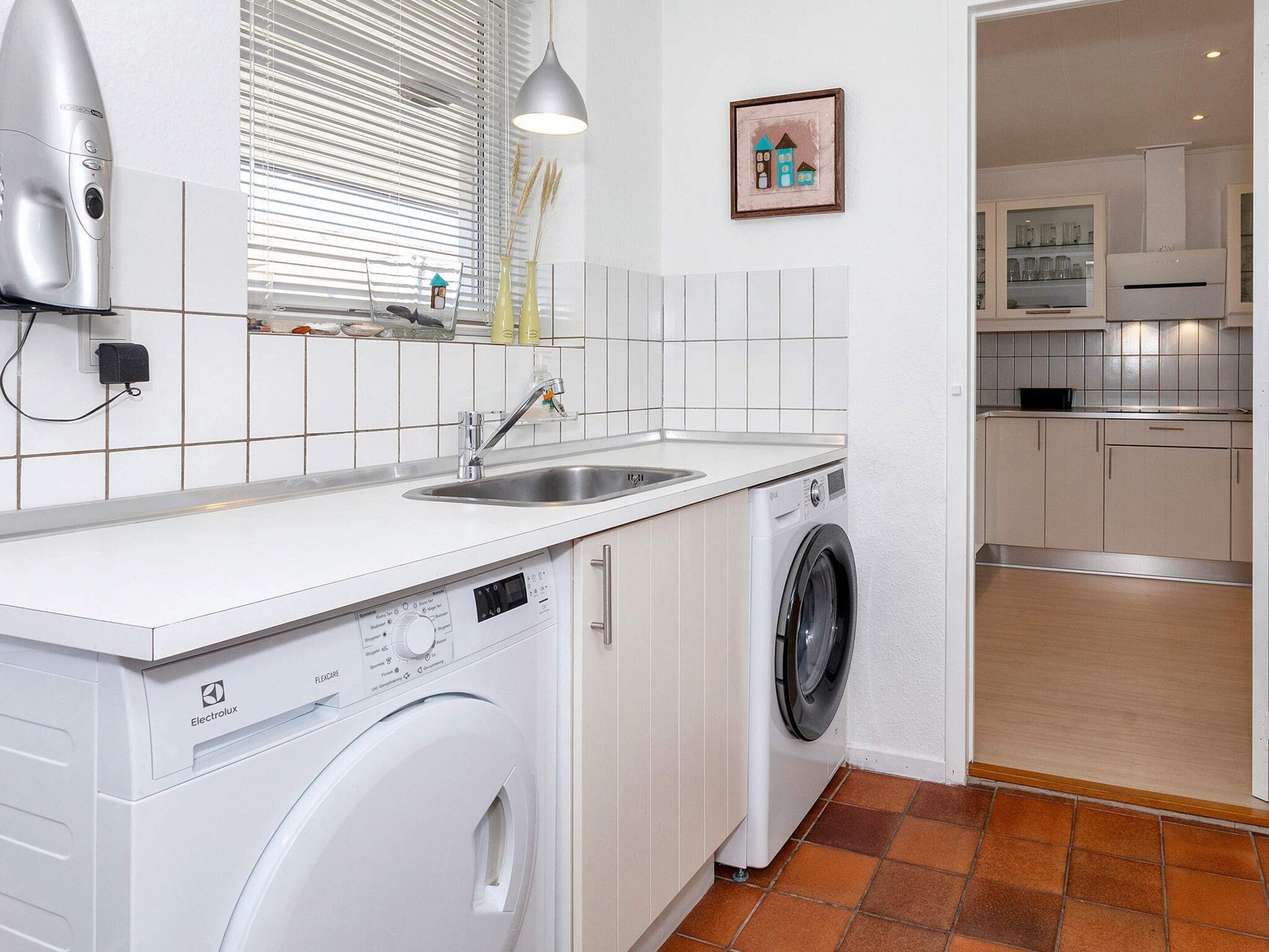 Une petite cuisine équipée d’un lave-linge, d’un évier et d’une fenêtre avec des stores.