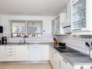 A modern kitchen with white cabinetry, a dishwasher, a built-in oven, and a window with blinds.