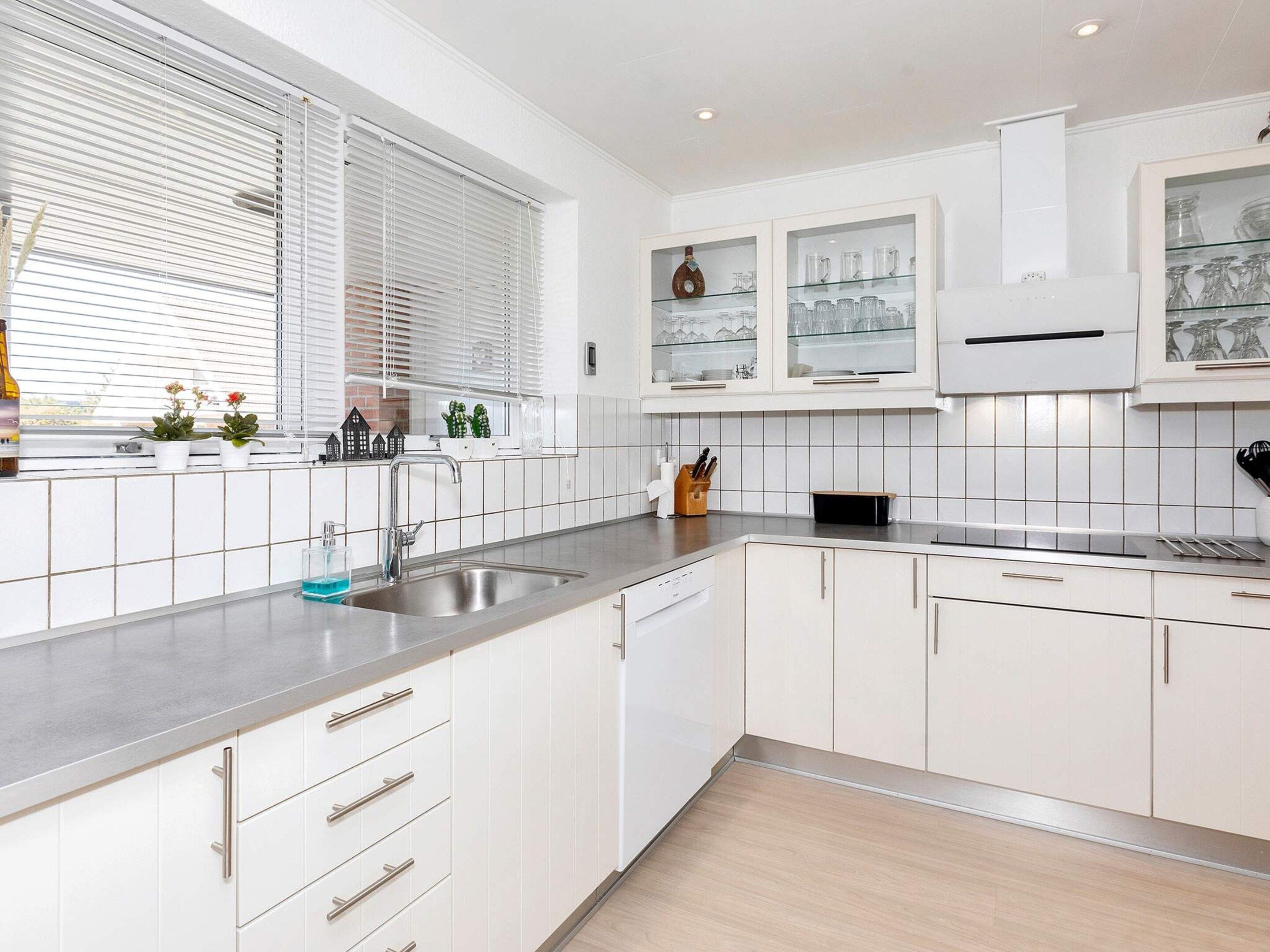 A modern kitchen with white cabinetry, a stainless steel sink, and a window with blinds.