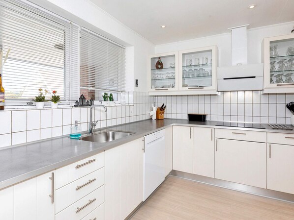 Una cocina moderna con armarios blancos, un lavamanos de acero inoxidable y una ventana con persianas.