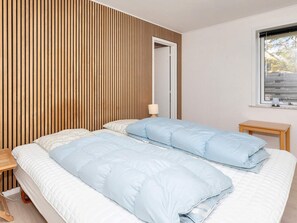 A bedroom with two beds, a wooden slat wall, a bedside table, and a window with a view. - 4 Star Holiday Home in Blokhus (Blokhus)
