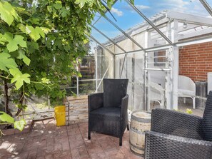 A greenhouse with a brick floor, black wicker furniture, and green grapevines.
