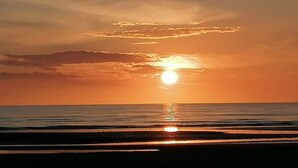 Auringonlasku meren yllä, kirkas taivas ja tyyni vesi.