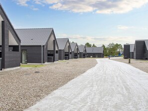 Une rangée de cabanes modernes aux couleurs sombres et aux toits en pente, disposées le long d’une allée de gravier.