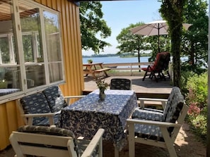 A covered patio with a table and chairs, a view of a lake, and a wooden deck. - 4 Star Holiday Home in Ramdala (Ramdala)