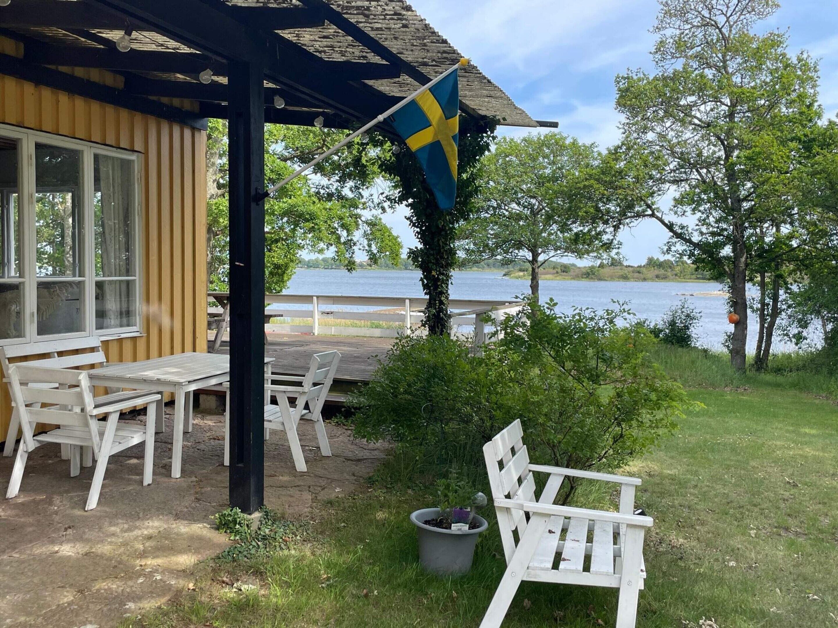 Ein Holzgebäude mit einer Flagge, Außenbereich zum Sitzen und Blick auf einen See.