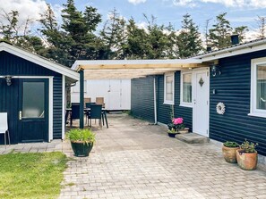 A covered patio area with a table and chairs, surrounded by potted plants and a wooden pergola. - 6 Person Holiday Home in Lokken (Lokken)