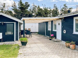 A covered patio area with a table and chairs, surrounded by potted plants and a wooden pergola. - 6 Person Holiday Home in Lokken (Lokken)