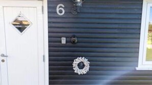 A house number '6' on a dark blue garage door, a white door with a diamond-shaped window, and a wreath decoration.