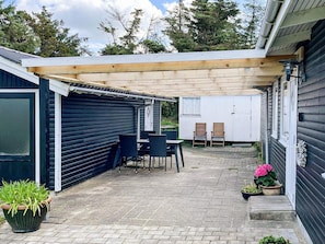 A covered patio area with a table and chairs, a potted plant, and a small garden. - 6 Person Holiday Home in Lokken (Lokken)