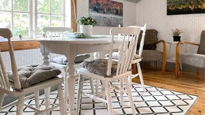 A dining area with a white table and chairs, a patterned rug, and a painting on the wall. - 4 Person Holiday Home in Kolmarden (Kolmården)