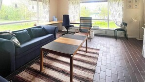 A cozy living room with a sofa, a small table, a chair, and a view of the outdoors through large windows. - 6 Person Holiday Home in Skummeslovsstrand (Skummesloevsstrand)