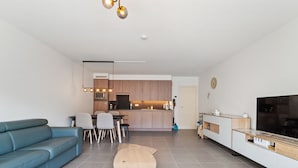 Una sala de estar moderna con un sofá azul, una mesa de centro de madera y un televisor sobre un mueble blanco.