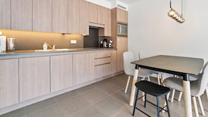 Una cocina moderna con armarios de madera, microondas integrado y una zona de comedor con mesa y sillas.