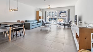 Una sala de estar moderna con comedor, un sofá, una mesa de centro y un balcón con vistas a la ciudad.