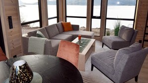 Ein gemütliches Blockhaus-Interieur mit einem großen Fenster, das Blick auf einen See und Berge gewährt.