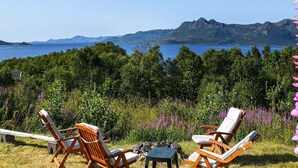 Blick auf die Küste mit Holzliegen und einem Tisch, mit Blick auf ein Gewässer und Berge.