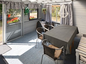 A covered patio area with a table and chairs, large windows with curtains, and a view of the outdoors.