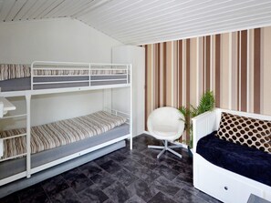 Een stapelbed met bureau en stoel, een bank en een gestreepte wand.