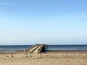 A beach with a wooden staircase leading to a pier extending into the water.
