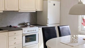 Une cuisine avec des meubles blancs, une cuisinière, un four, un réfrigérateur et une table à manger avec des chaises.