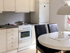 A kitchen with white cabinets, a stove, an oven, a refrigerator, and a dining table with chairs. - 10 Person Holiday Home in Skummeslovsstrand (Skummesloevsstrand)