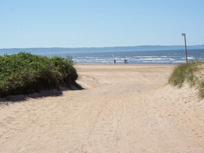 Een zandpad langs het strand dat uitkomt bij de zee, met een heldere lucht.