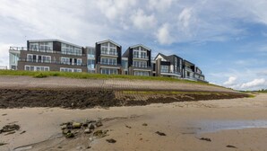 A modern multi-story building with large windows and balconies, situated on a sandy beach with a grassy embankment. - Seaside Escape, Sint-annaland (Sint-Annaland)