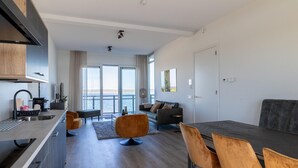 A modern, open-plan living and dining area with a kitchen, large windows, and a view of the sea. - Seaside Escape, Sint-annaland (Sint-Annaland)
