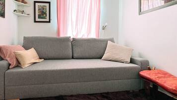 A grey sofa with two cushions, a small red bench, a furry rug, and a framed picture on the wall.