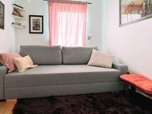 A grey sofa with two cushions, a small red bench, a furry rug, and a framed picture on the wall. - 4 Star Holiday Home in Sparreholm (Sparreholm)
