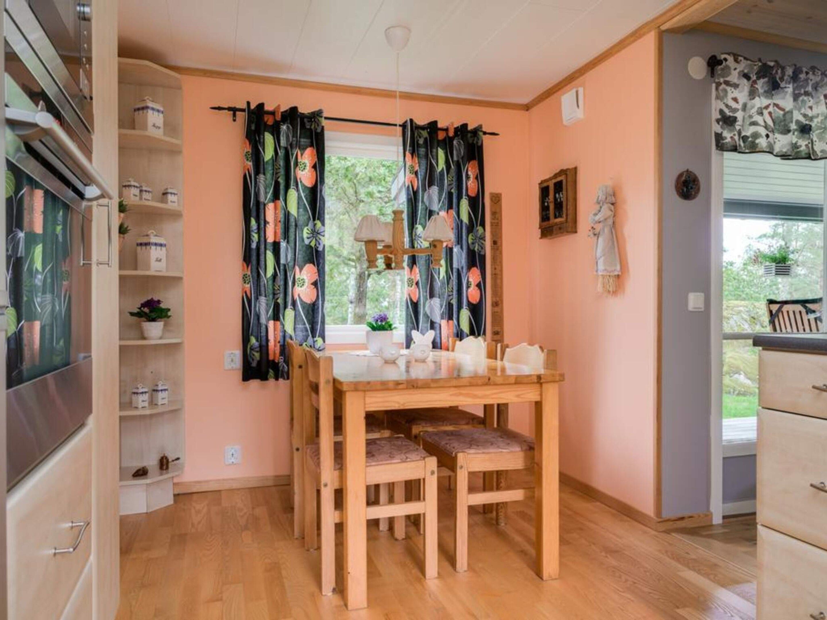 A cozy dining area with a wooden table and chairs, a window with curtains, and a view of greenery outside.